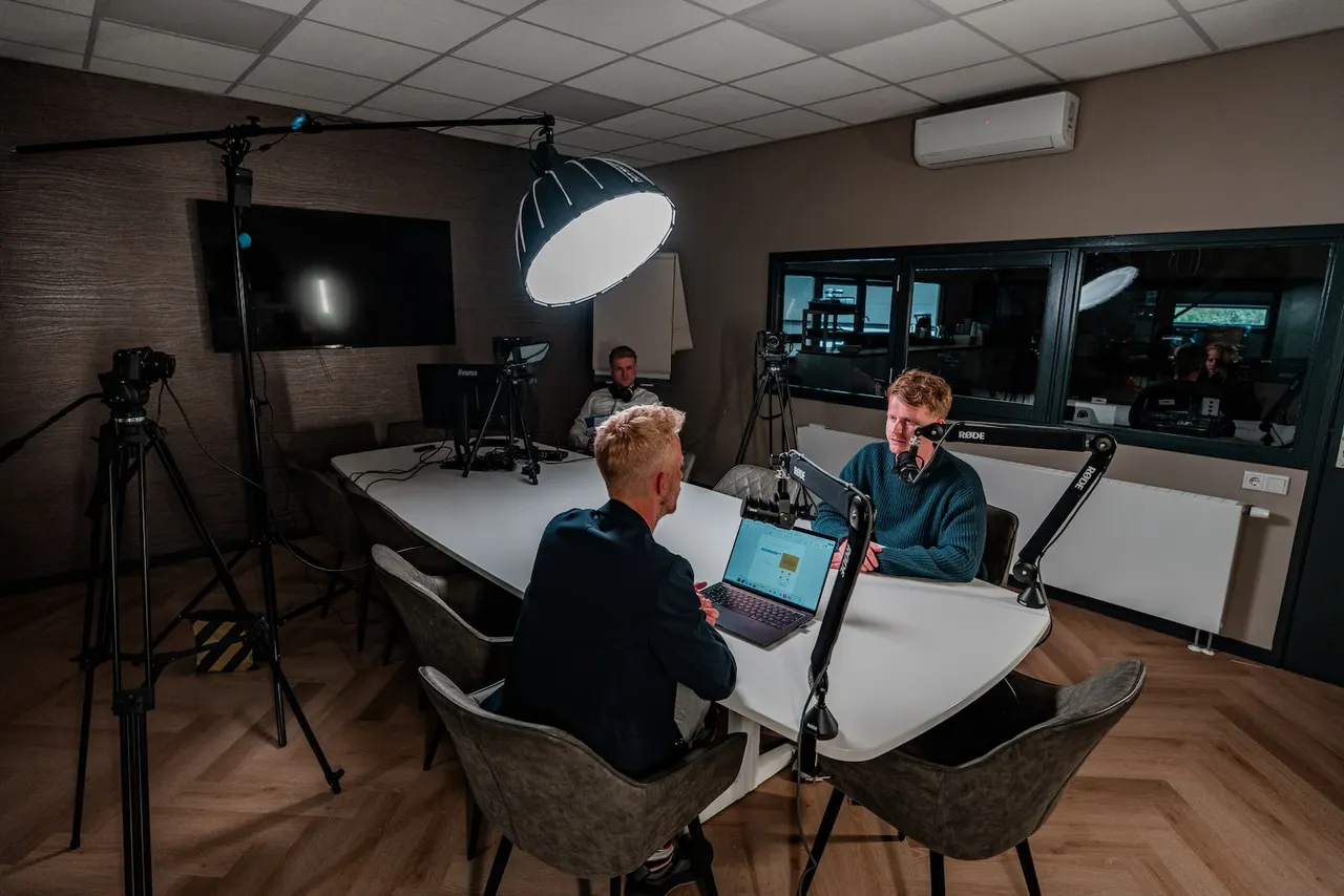 Opnamesessie met hosts en gast aan de studiotafel.