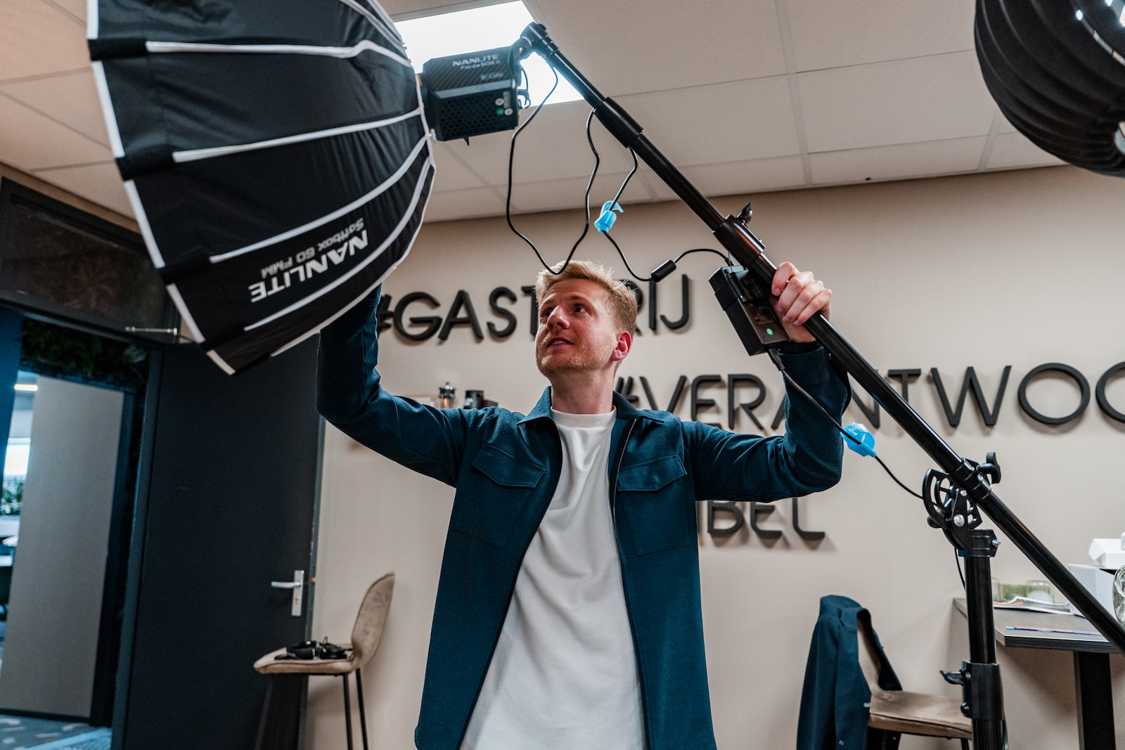 Jesse bouwt de mobiele studio op bij een opdrachtgever: softbox, boom-microfoon en camera in een vergaderruimte.